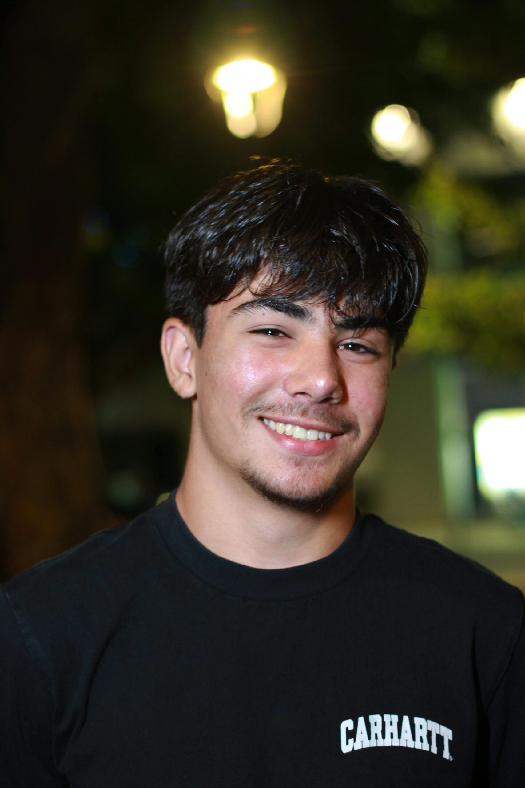 Portrait of a young man smiling outdoors at night with bokeh background.