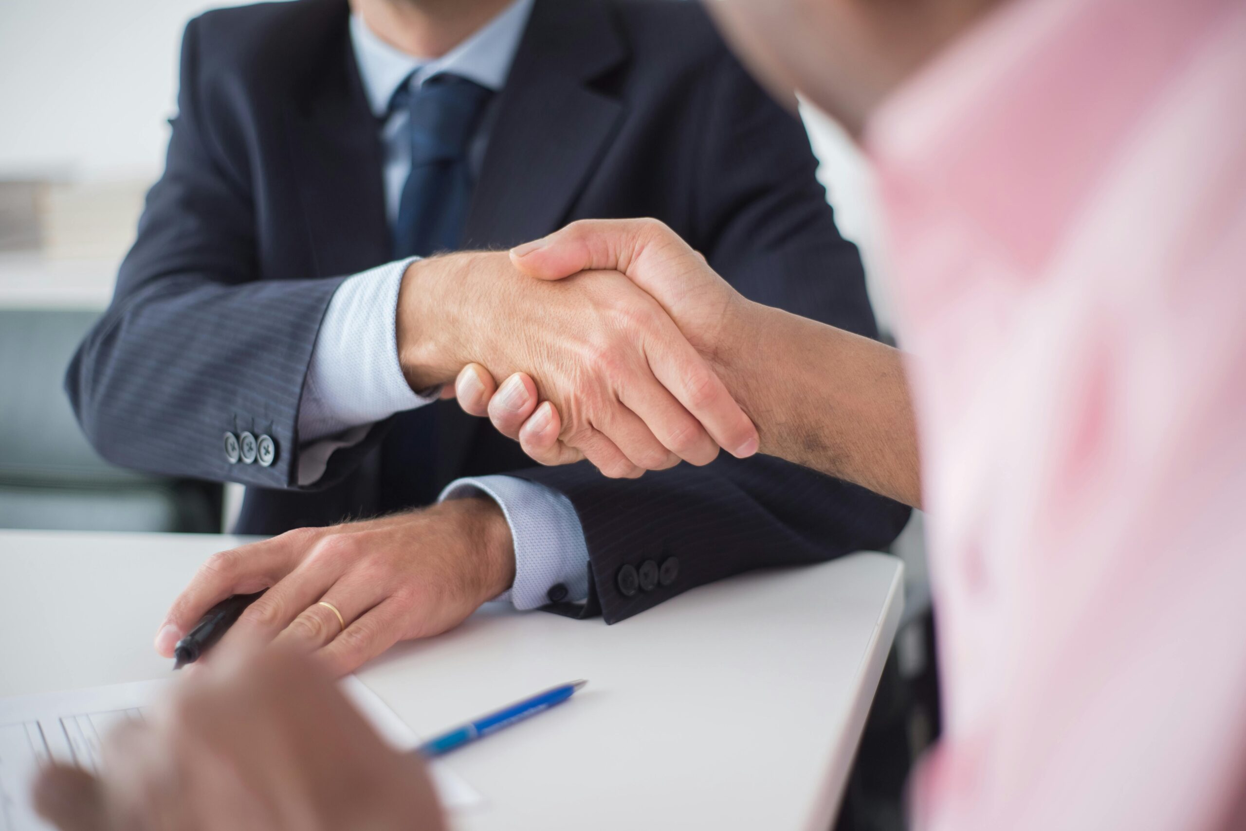 pexels-photo-8441790-8441790 Two businessmen shaking hands across table, symbolizing agreement and partnership in an office environment.