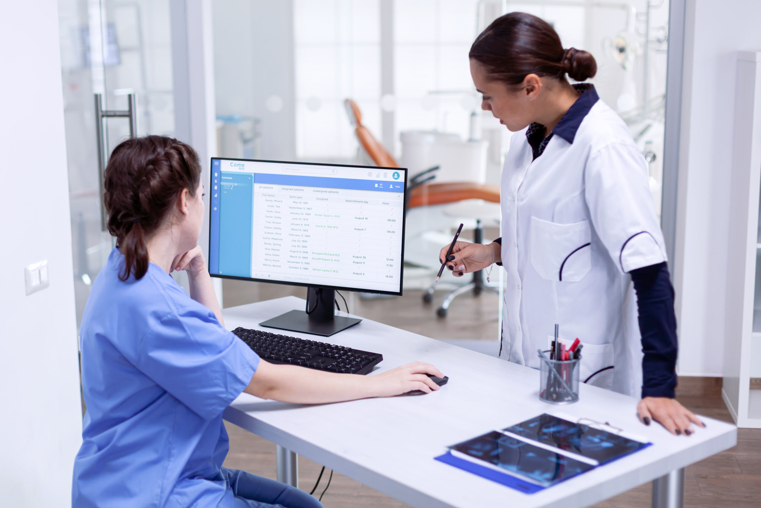 Stomatolog and nurse in tooth clinic checking patient appointment. Stomatolog and nurse in tooth clinic checking patient appointment looking at computer monitor. Stomatology assistant and teeth doctor discussing in reception of dental office